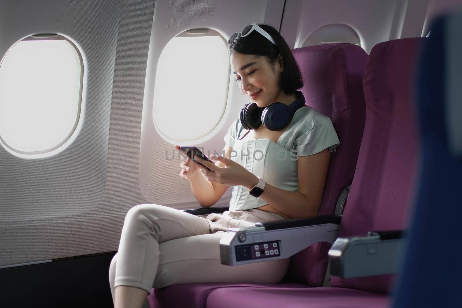 Young woman sitting with phone on the aircraft seat near the window during the flight in the airplane by wichayada