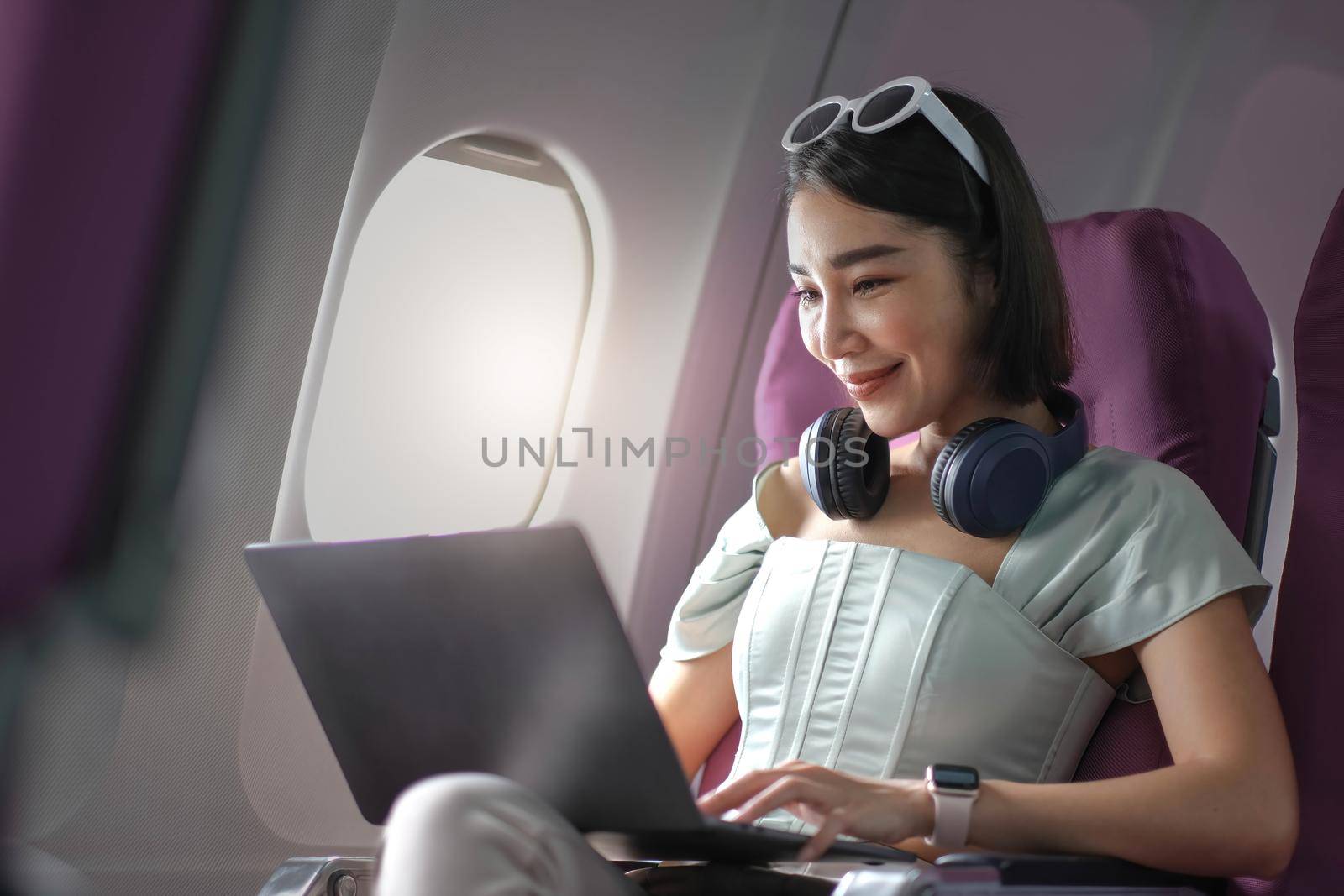 Asian young woman using laptop sitting near windows at first class on airplane during flight,Traveling and Business concept.