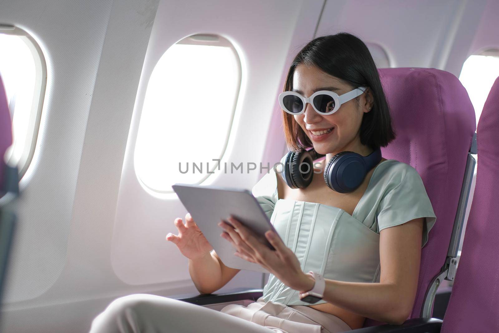 Travel tourism with modern technology and air flights concept, woman sitting in plane with modern digital gadget and searching favourite music playlist in application for listening.