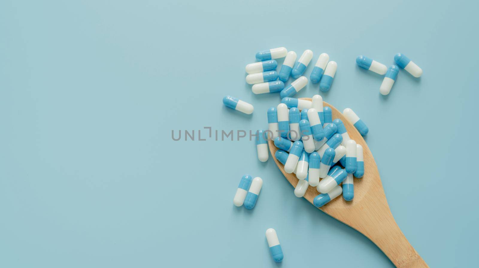 Blue-white antibiotic capsule pills on wooden spoon and blue background. Antibiotic drug resistance. Prescription drug. Medical care. Pharmaceutical care. Antimicrobial drug. World Pharmacist Day. by Fahroni