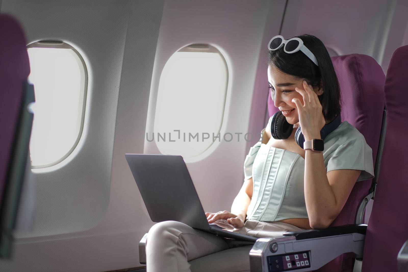 Asian young woman using laptop sitting near windows at first class on airplane during flight,Traveling and Business concept by wichayada