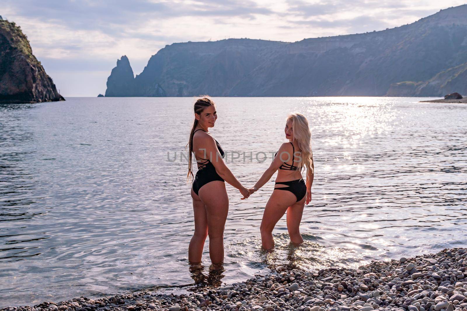 Two beautiful lgbt lesbian female friends relax and happy at the beach sitting on the sand wearing swimsuit. Travel and sea on holiday vacation