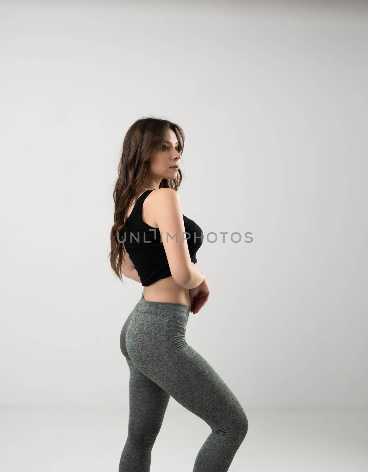 Sporty young woman in sport outfit, tight black leggings and top isolated in black wall