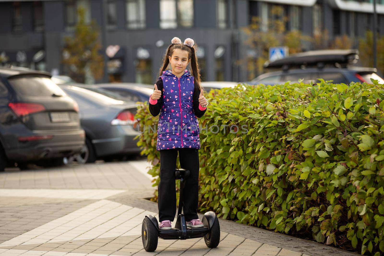 Happy little girl standing on electric scooter outdoor.