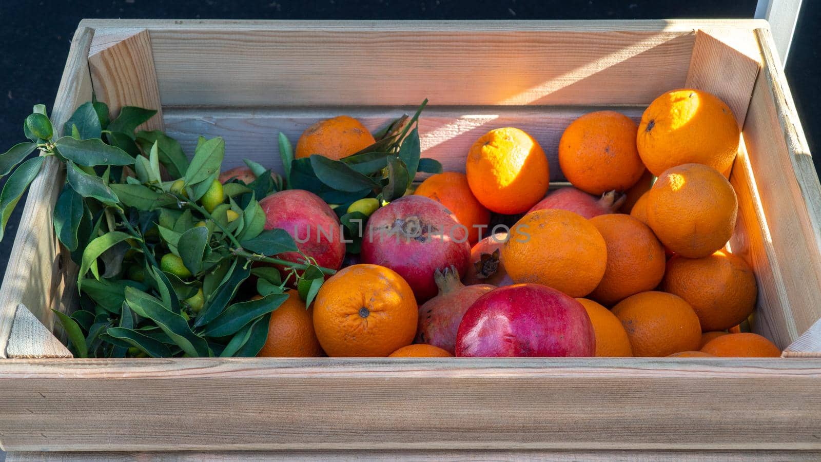 Oranges and pomegranates in a wooden box under the rays of the sun. High quality photo
