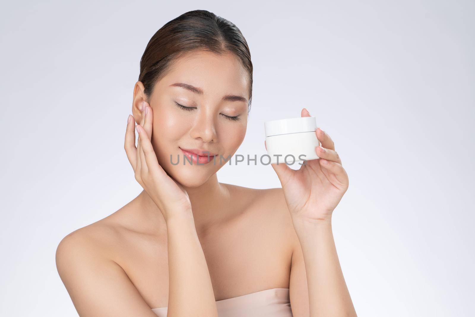 Gorgeous woman smiling holding mockup product for advertising text place, light grey background. Concept of healthcare for skin, beauty care product for advertising.