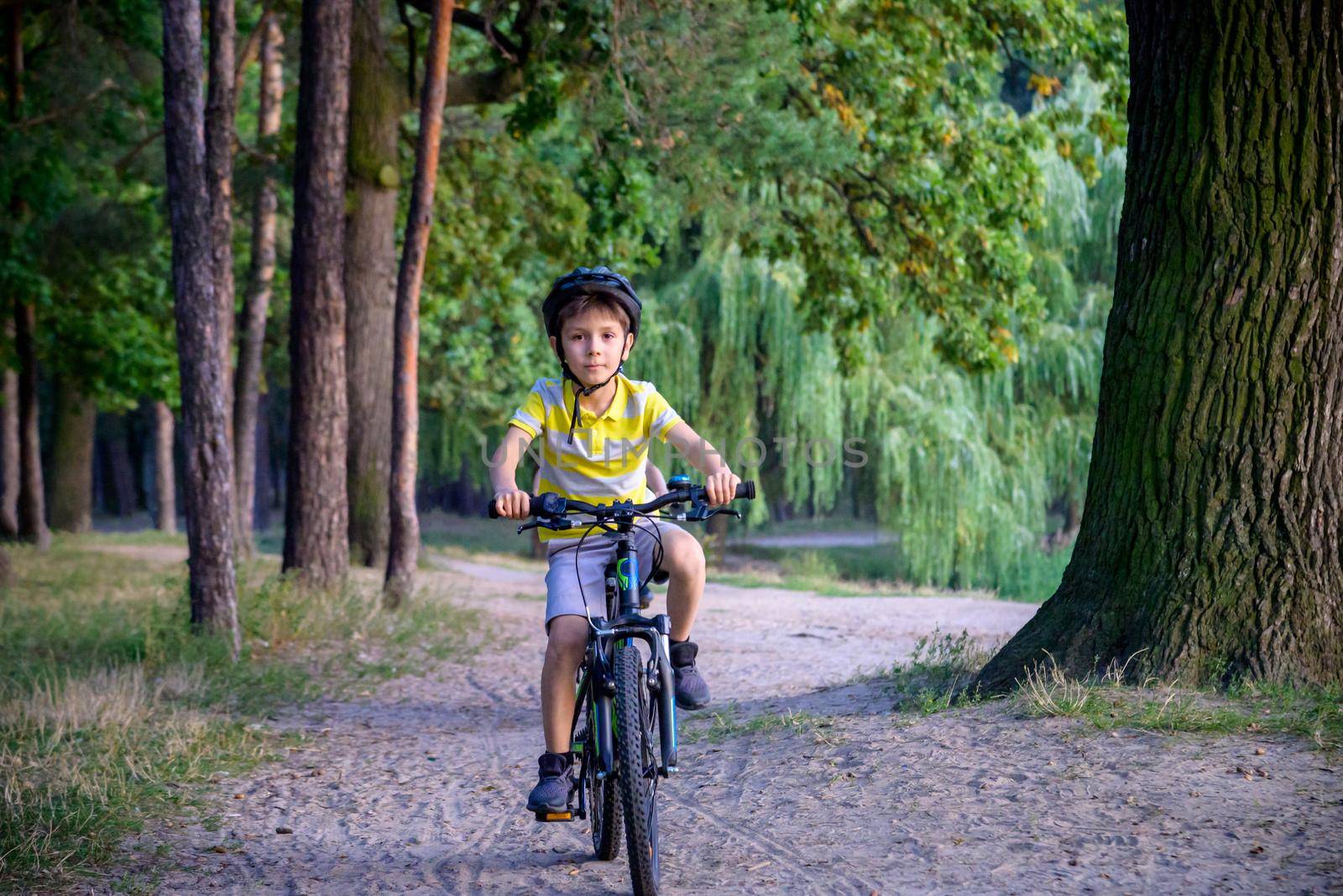 Portrait of happy toddler child boy riding on bike with helmet. He rides from a small hill, through a sandy forest path. Sport concept: kids ride bicycle first bike active toddler kid by Kobysh