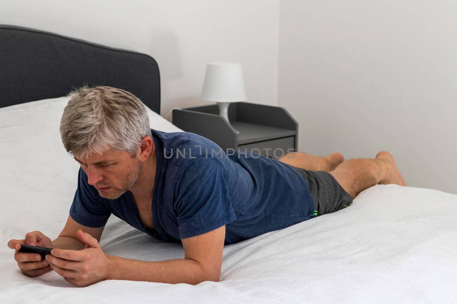 Shot of a mid aged man laying on the bed and looking trough his phone