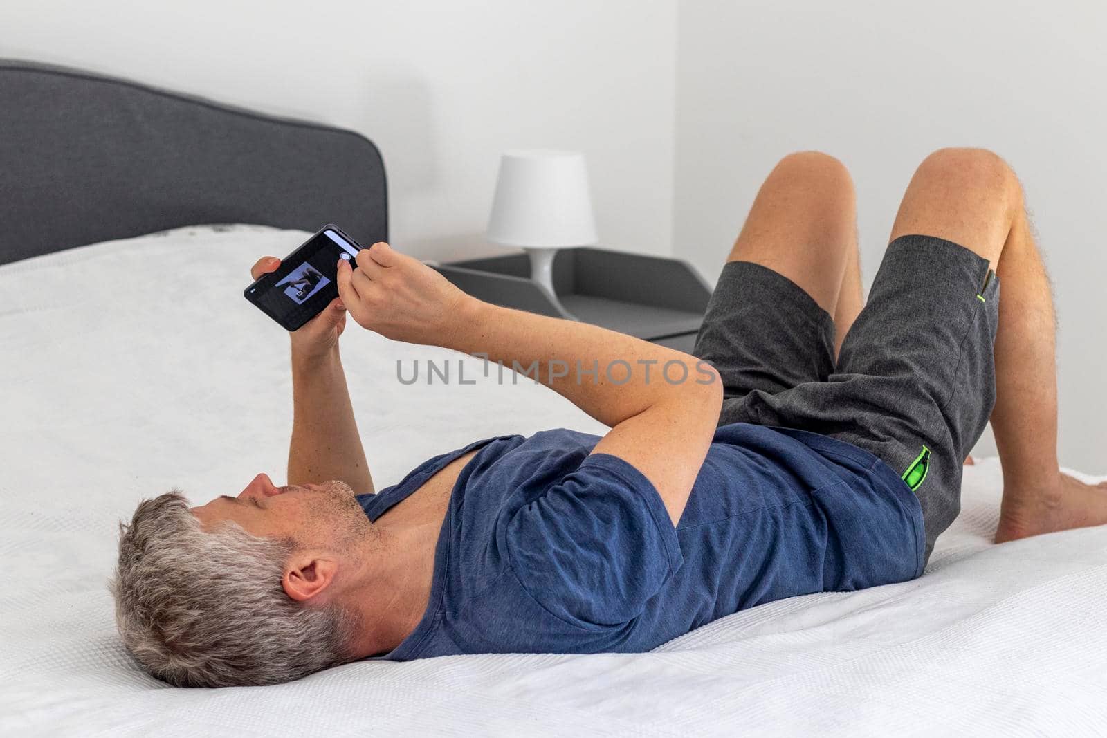 Shot of a mid aged man laying on the bed and looking trough his phone