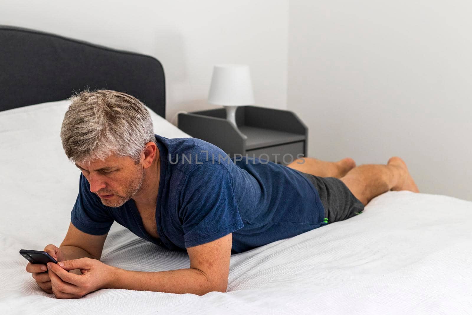 Shot of a mid aged man laying on the bed and looking trough his phone
