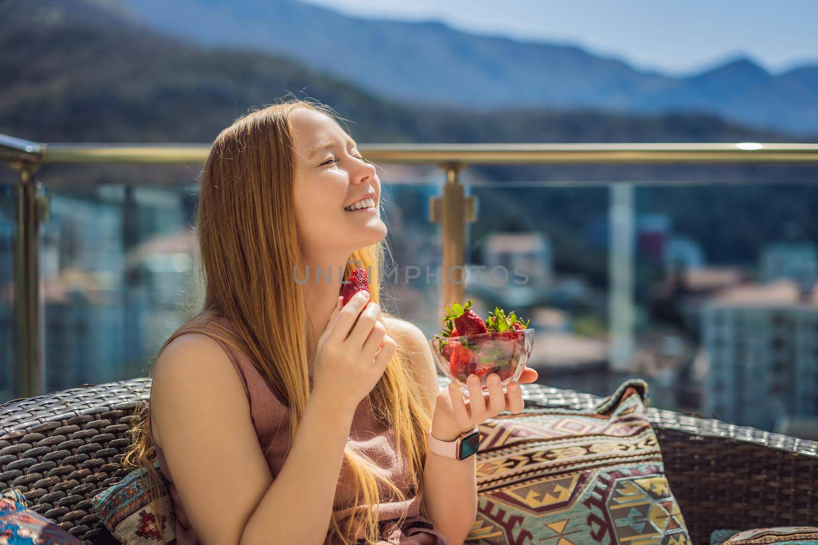 Portrait of gorgeous woman wearing beautiful dress sitting in a patio and eating strawberry.