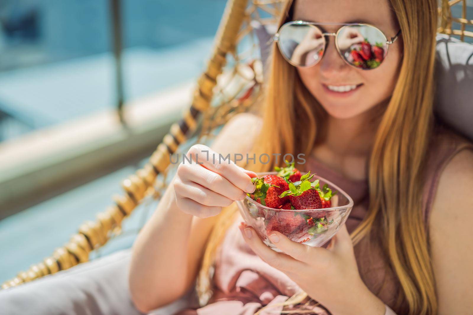 Portrait of gorgeous woman wearing beautiful dress sitting in a patio and eating strawberry.