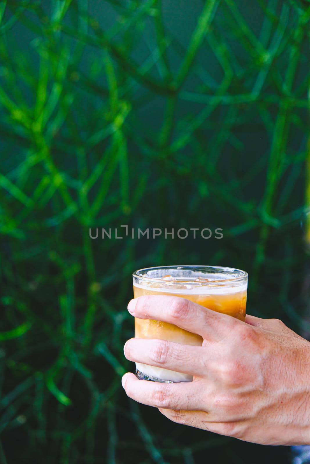 Hand hold iced latte coffee in a  tall glass. cold summer drink  with green nature background