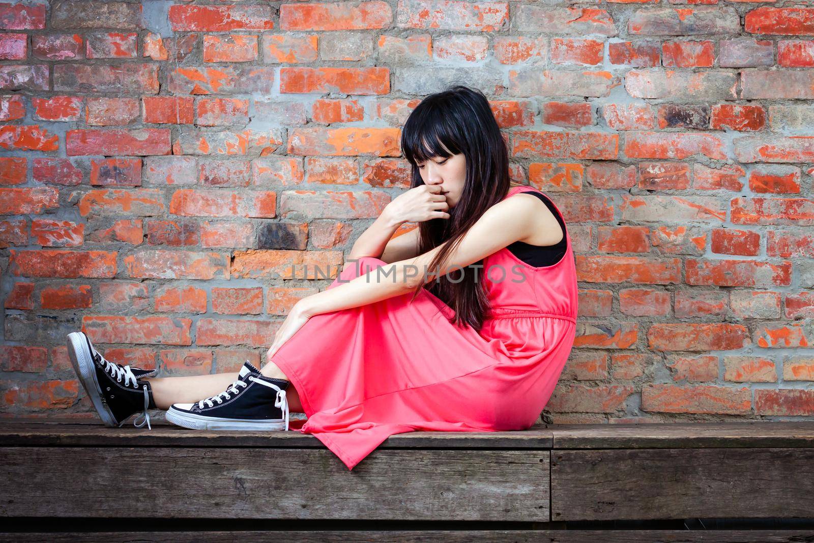 Young Asian woman sitting by red brick wall feeling depressed and sad