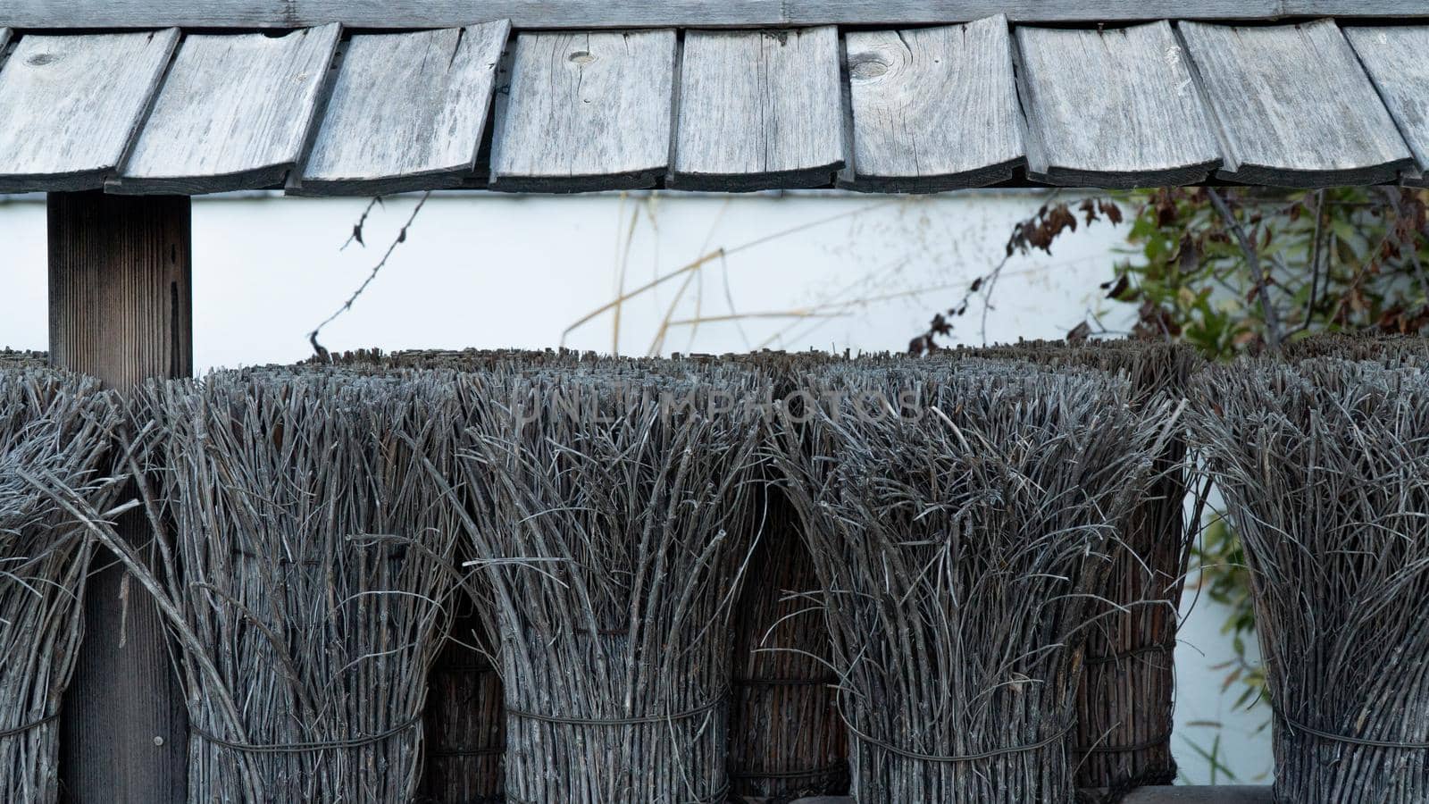 Decorative fence made of dry tree branches and wooden roof of a village house. High quality photo