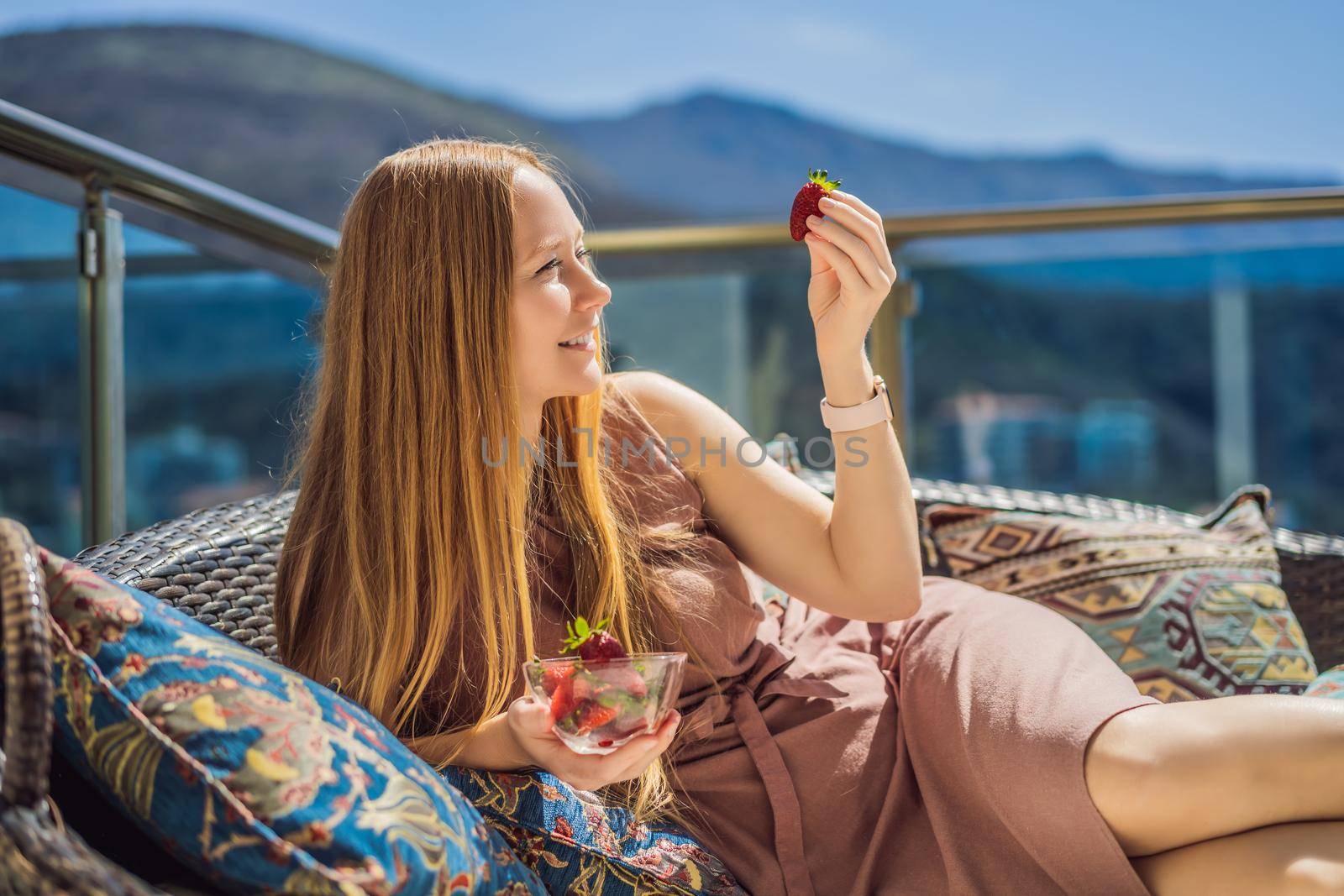 Portrait of gorgeous woman wearing beautiful dress sitting in a patio and eating strawberry.
