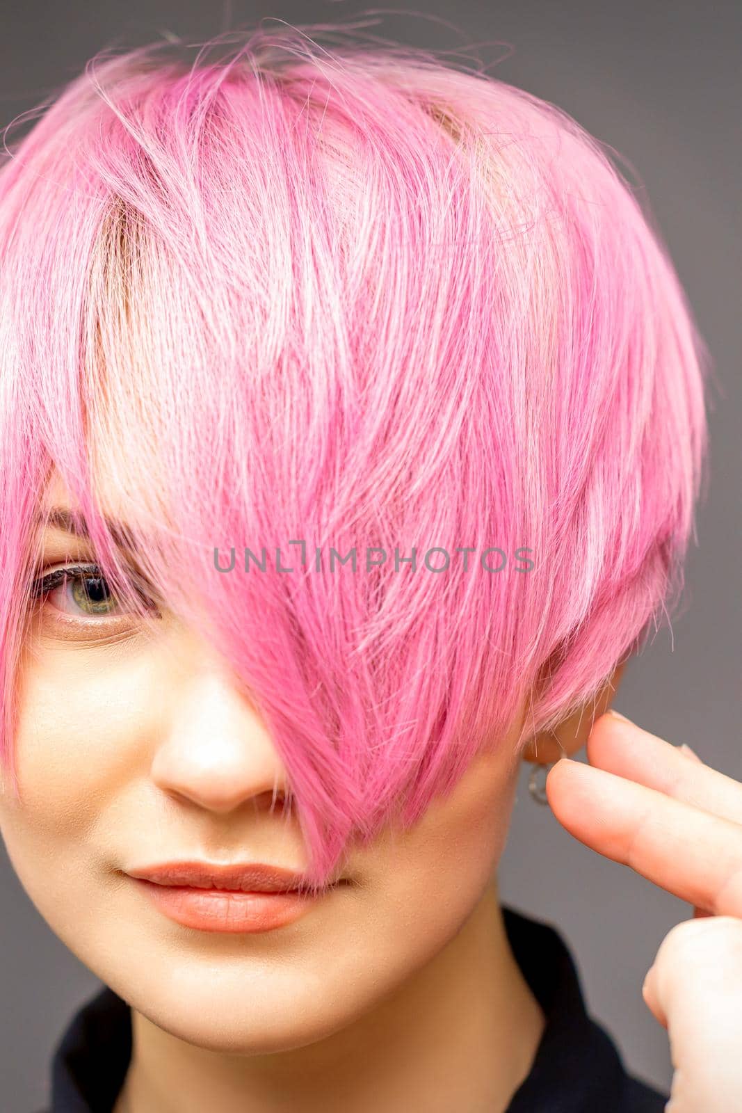 Hairdresser with hands and comb is checking out and fixing the short pink hairstyle of the young white woman in a hair salon. by okskukuruza