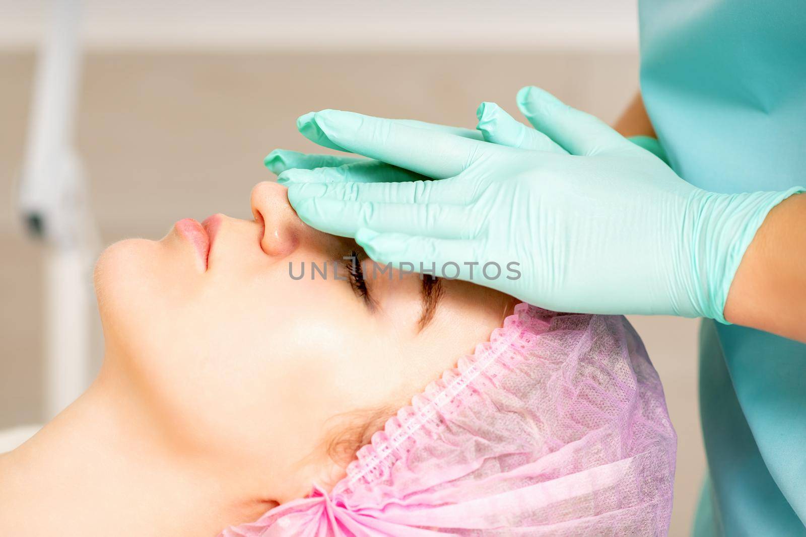 Cosmetologist with gloved hands applies a moisturizing mask with peeling cream on the female face. Facial cosmetology treatment. Procedures for facial care