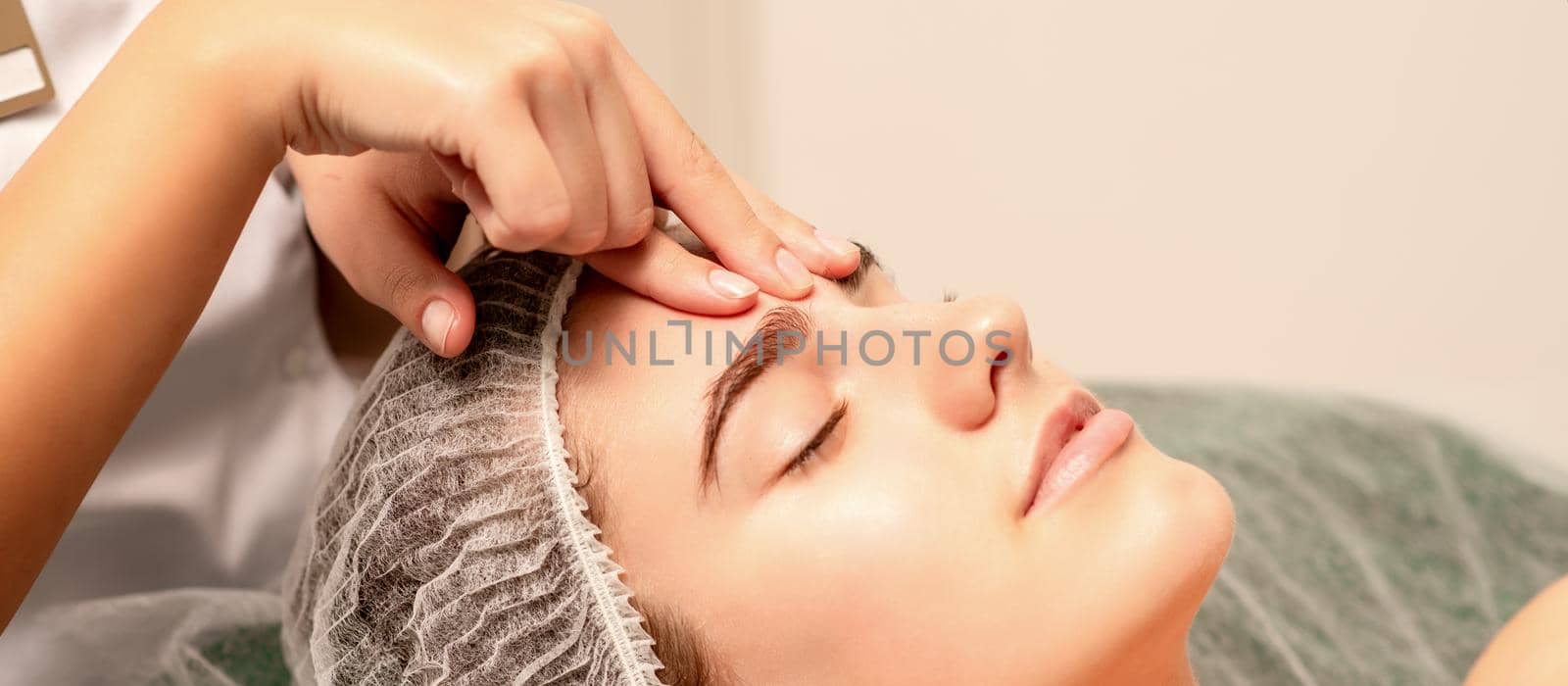 Beautiful caucasian young woman receiving a facial massage with closed eyes in spa salon, close up. Relaxing treatment concept. by okskukuruza