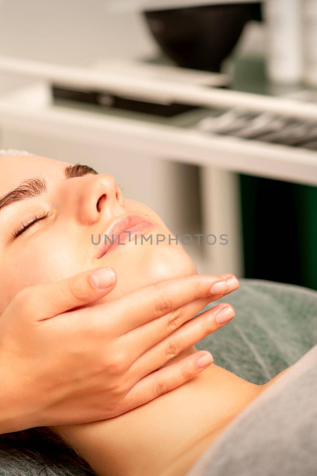 Facial massage. Hands of a masseur massaging neck of a young caucasian woman in a spa salon, the concept of health massage. by okskukuruza