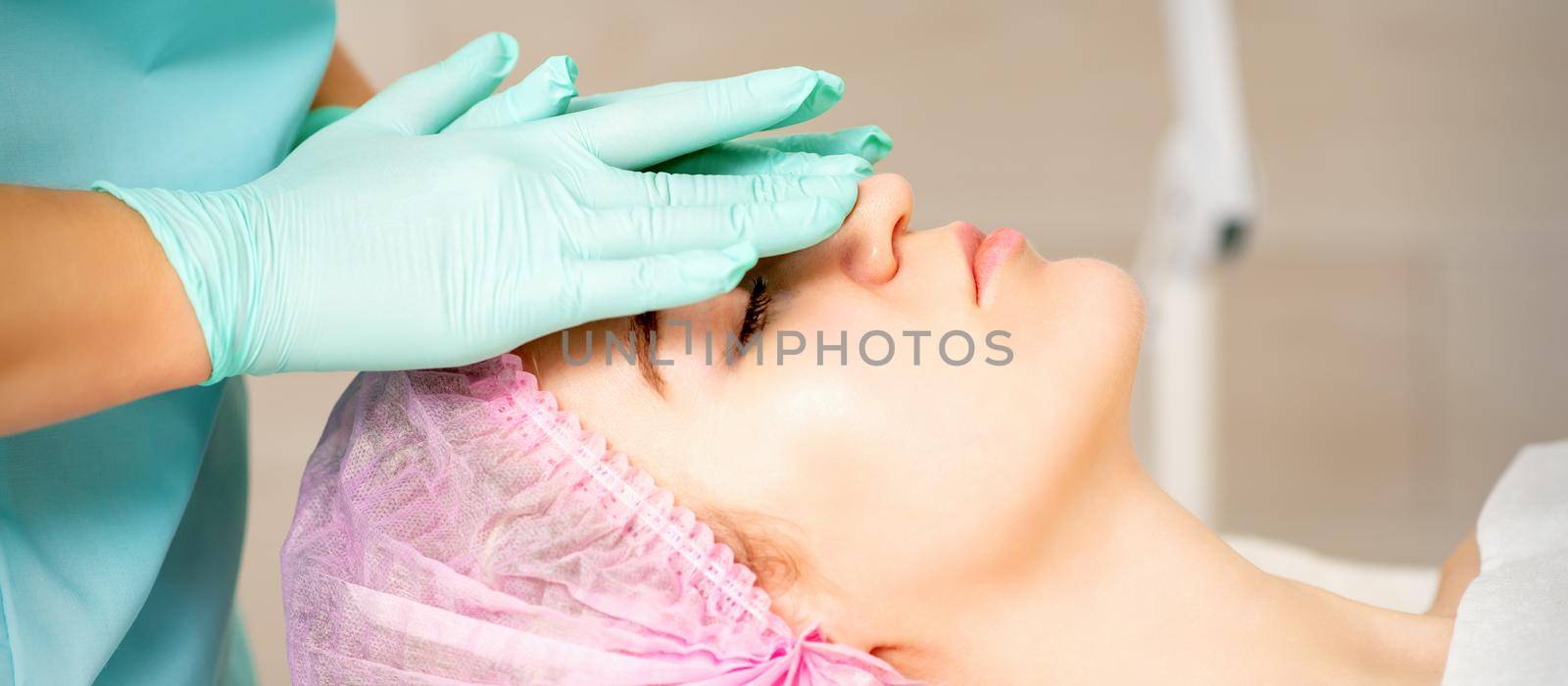 Cosmetologist with gloved hands applies a moisturizing mask with peeling cream on the female face. Facial cosmetology treatment. Procedures for facial care