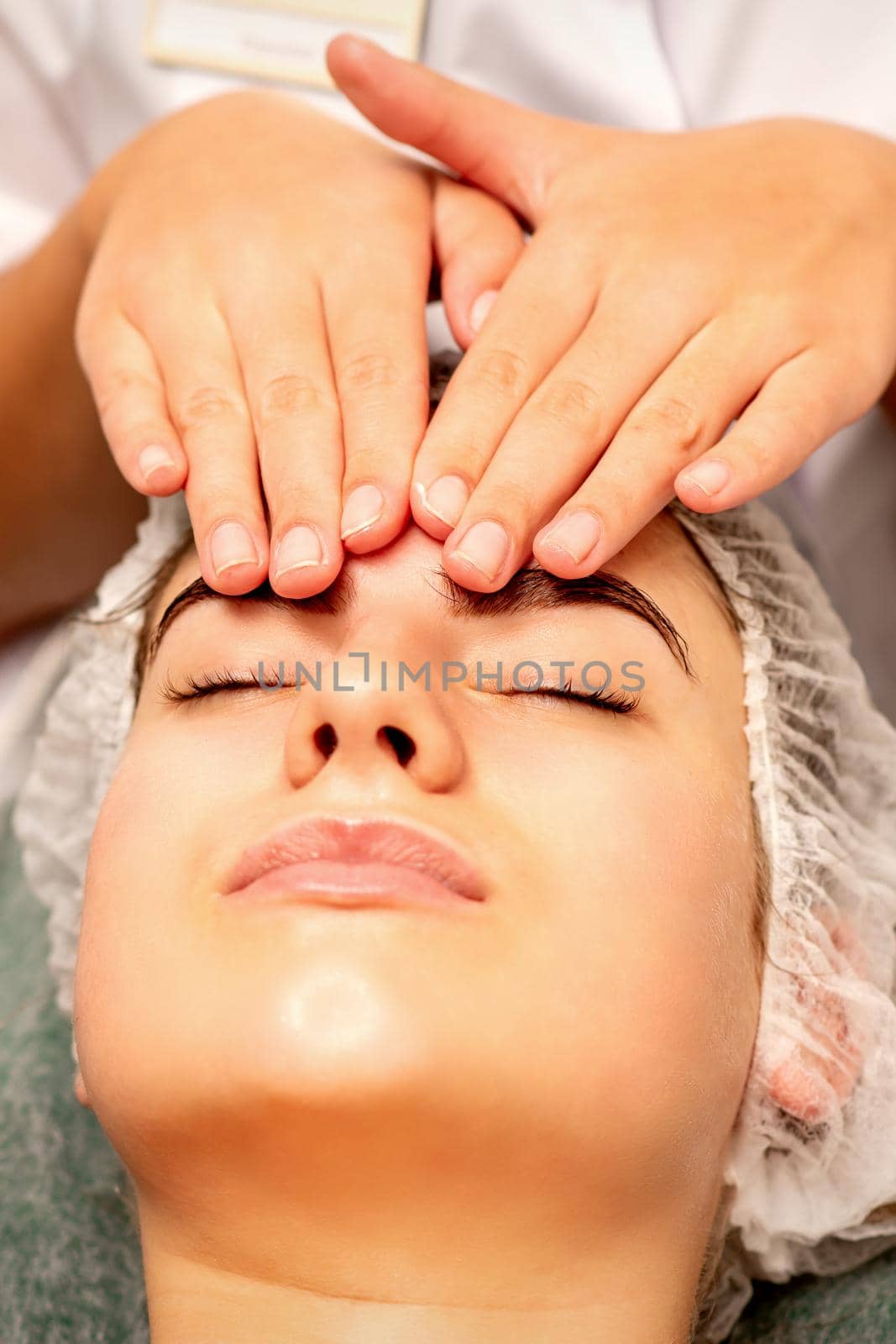 Head massage. Beautiful caucasian young white woman receiving a head and forehead massage with closed eyes in a spa salon. by okskukuruza