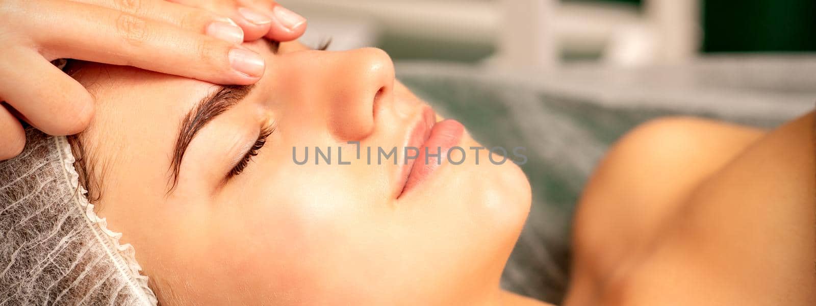 Head massage. Beautiful caucasian young white woman receiving a head and forehead massage with closed eyes in a spa salon. by okskukuruza