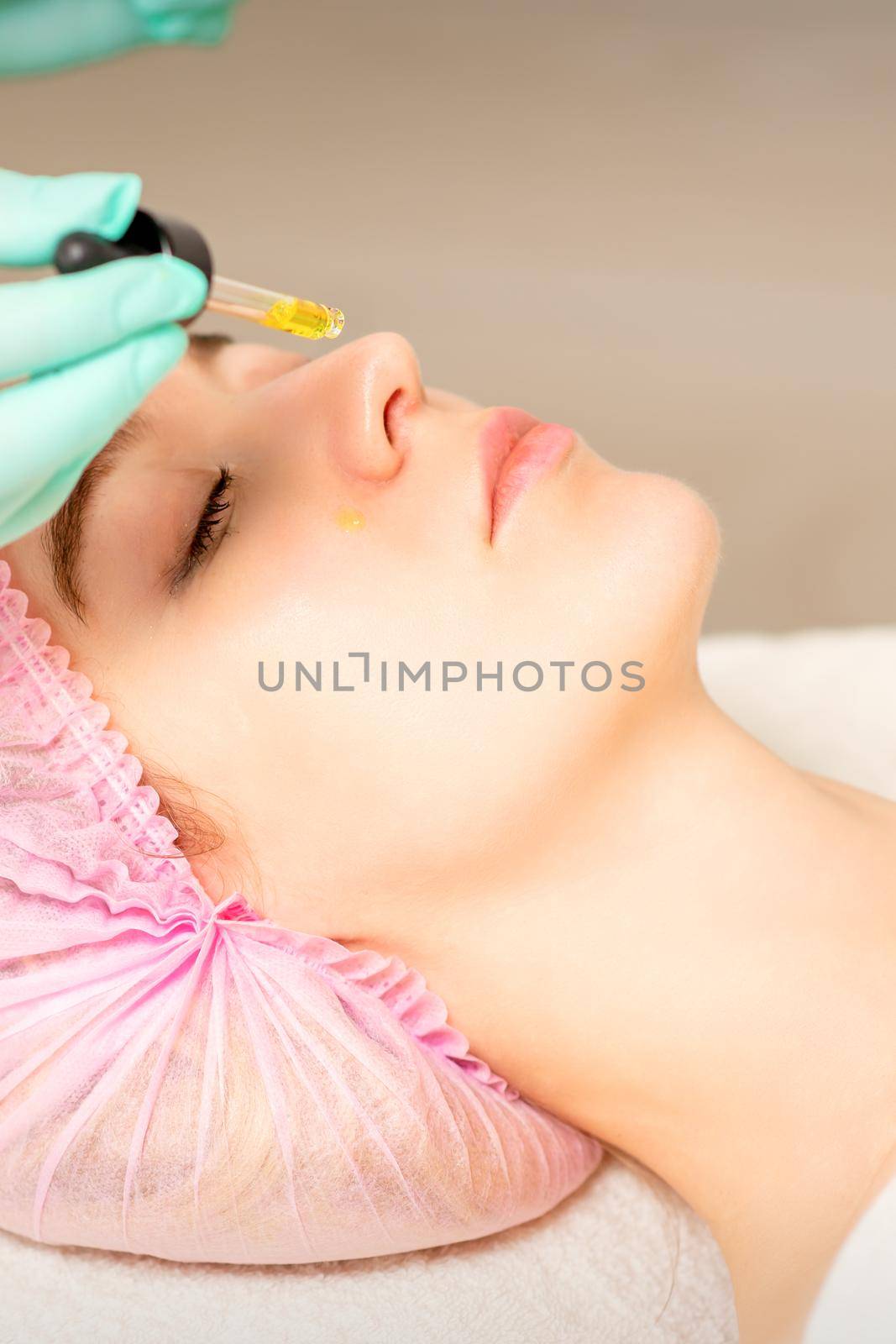 Young white woman getting acid organic retinol peel face skin with the pipette in a beauty clinic