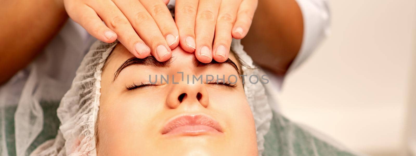 Head massage. Beautiful caucasian young white woman receiving a head and forehead massage with closed eyes in a spa salon. by okskukuruza