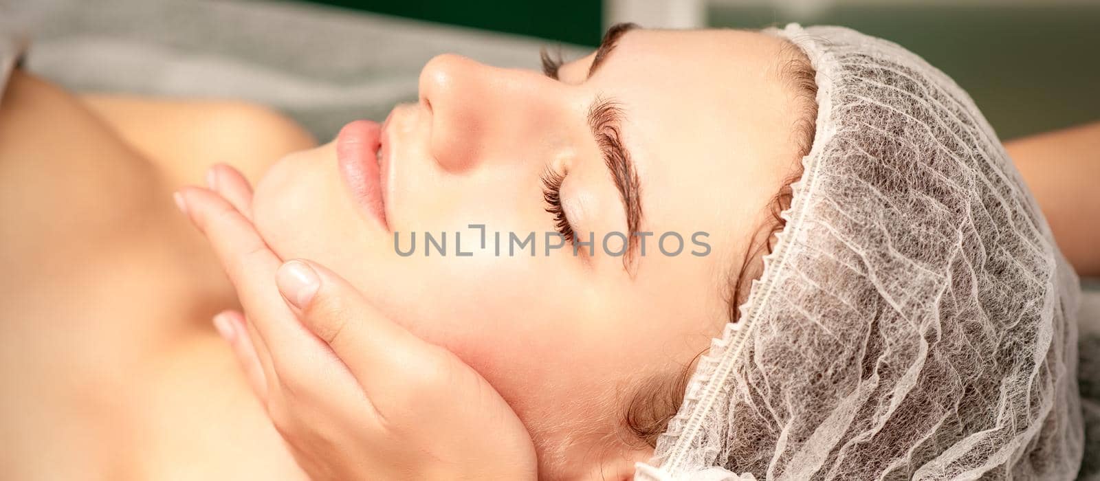 Facial massage. Hands of a masseur massaging neck of a young caucasian woman in a spa salon, the concept of health massage. by okskukuruza