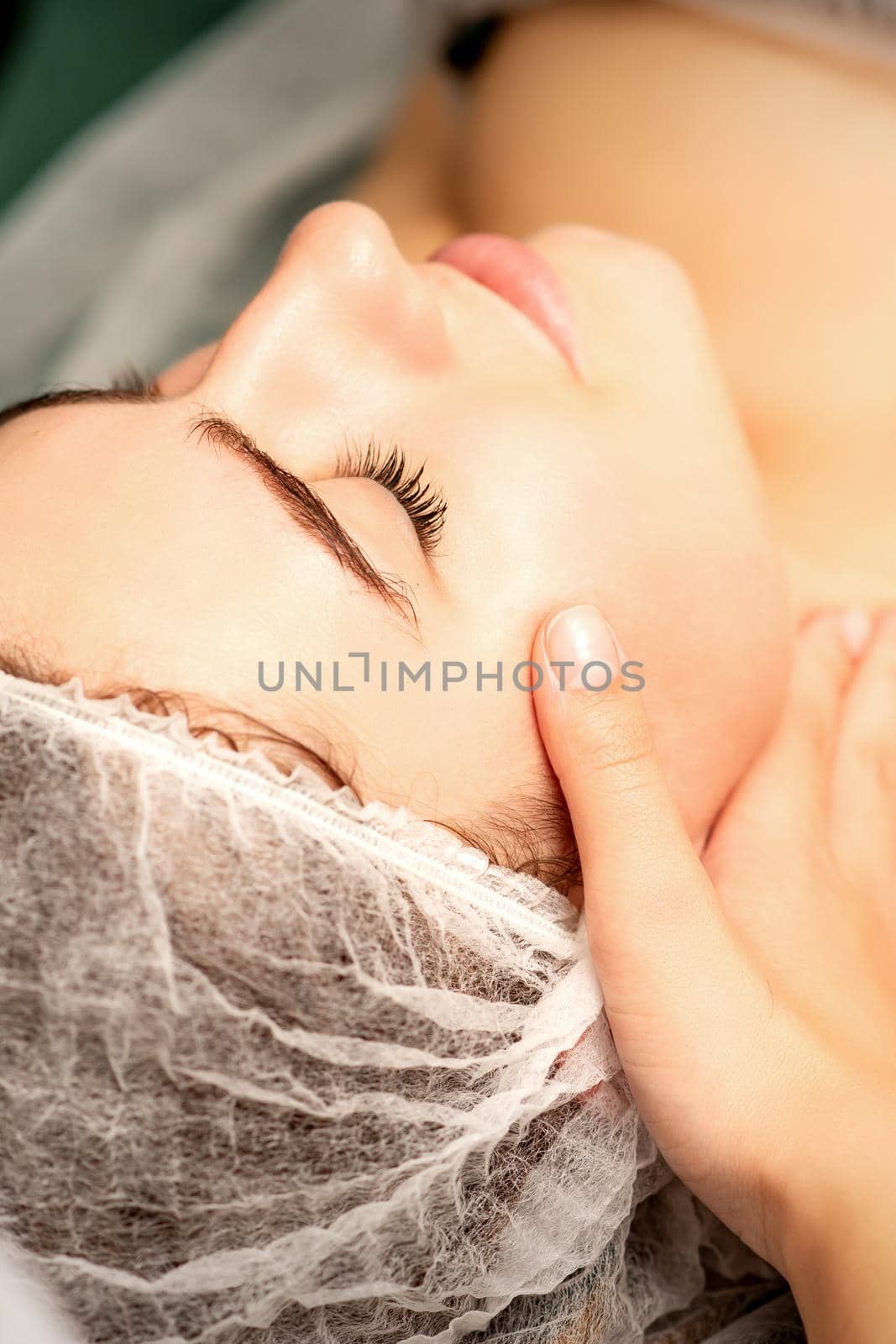 Facial massage. Hands of a masseur massaging neck of a young caucasian woman in a spa salon, the concept of health massage. by okskukuruza