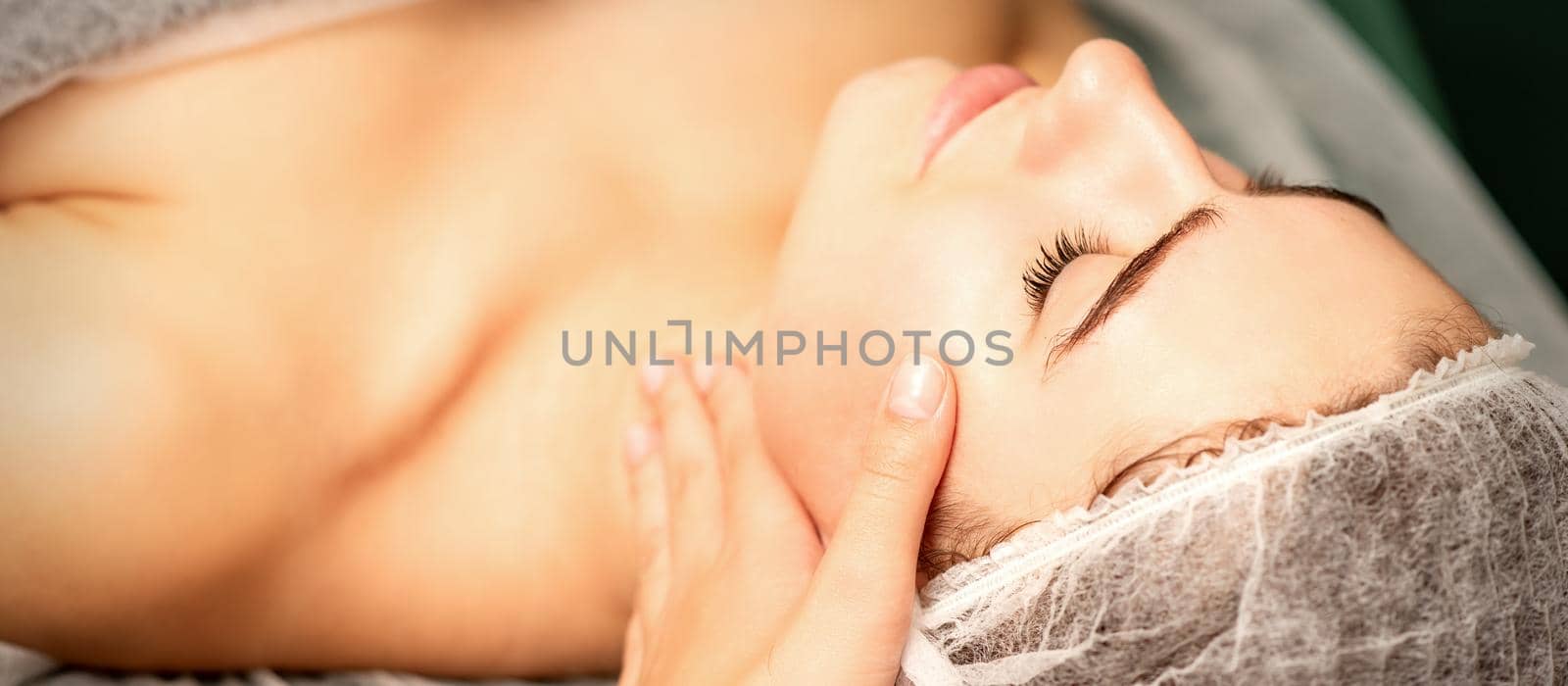 Facial massage. Hands of a masseur massaging neck of a young caucasian woman in a spa salon, the concept of health massage. by okskukuruza