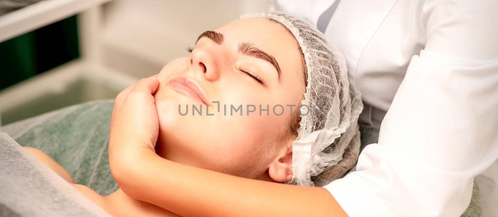 Facial massage. Hands of a masseur massaging neck of a young caucasian woman in a spa salon, the concept of health massage. by okskukuruza