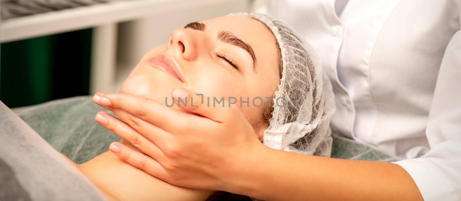 Facial massage. Hands of a masseur massaging neck of a young caucasian woman in a spa salon, the concept of health massage. by okskukuruza