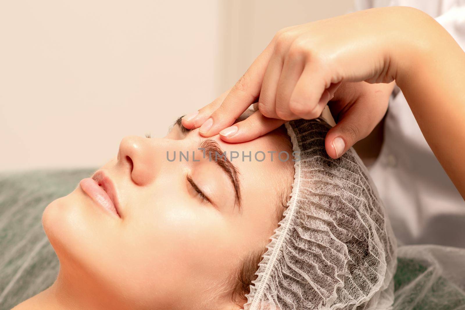 Beautiful caucasian young woman receiving a facial massage with closed eyes in spa salon, close up. Relaxing treatment concept