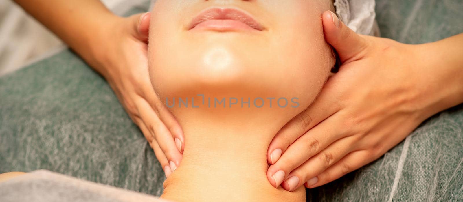 Facial massage. Hands of a masseur massaging neck of a young caucasian woman in a spa salon, the concept of health massage. by okskukuruza