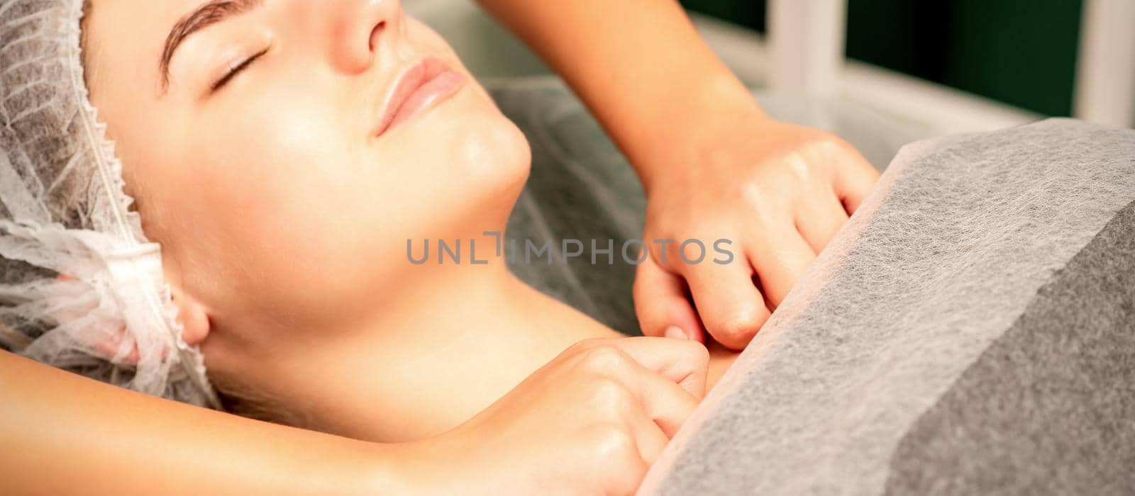 Massaging female breast, and shoulder. Young beautiful caucasian woman with closed eyes receiving chest and shoulders massage in beauty spa salon