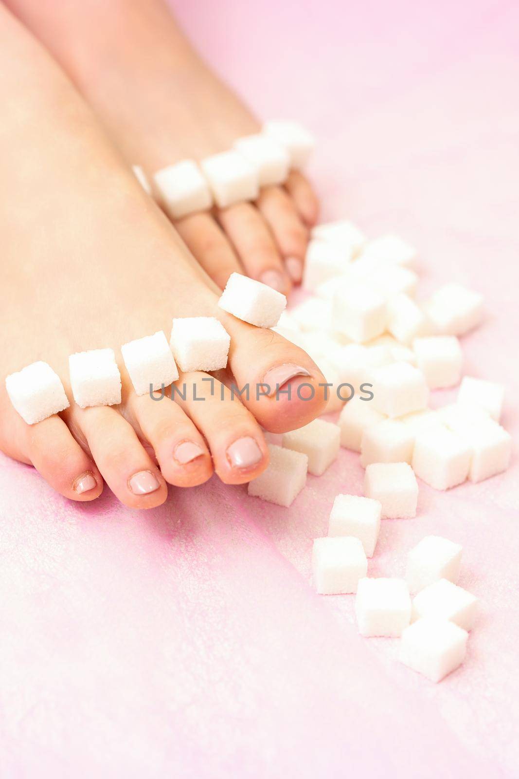 The concept of epilation, waxing. Sugar cubes lying down in a row on female feet, toes over pink background. by okskukuruza