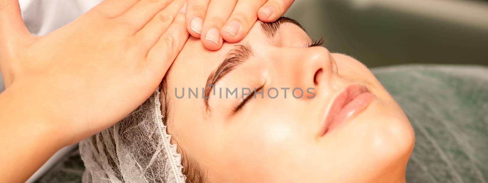 Head massage. Beautiful caucasian young white woman receiving a head and forehead massage with closed eyes in a spa salon. by okskukuruza