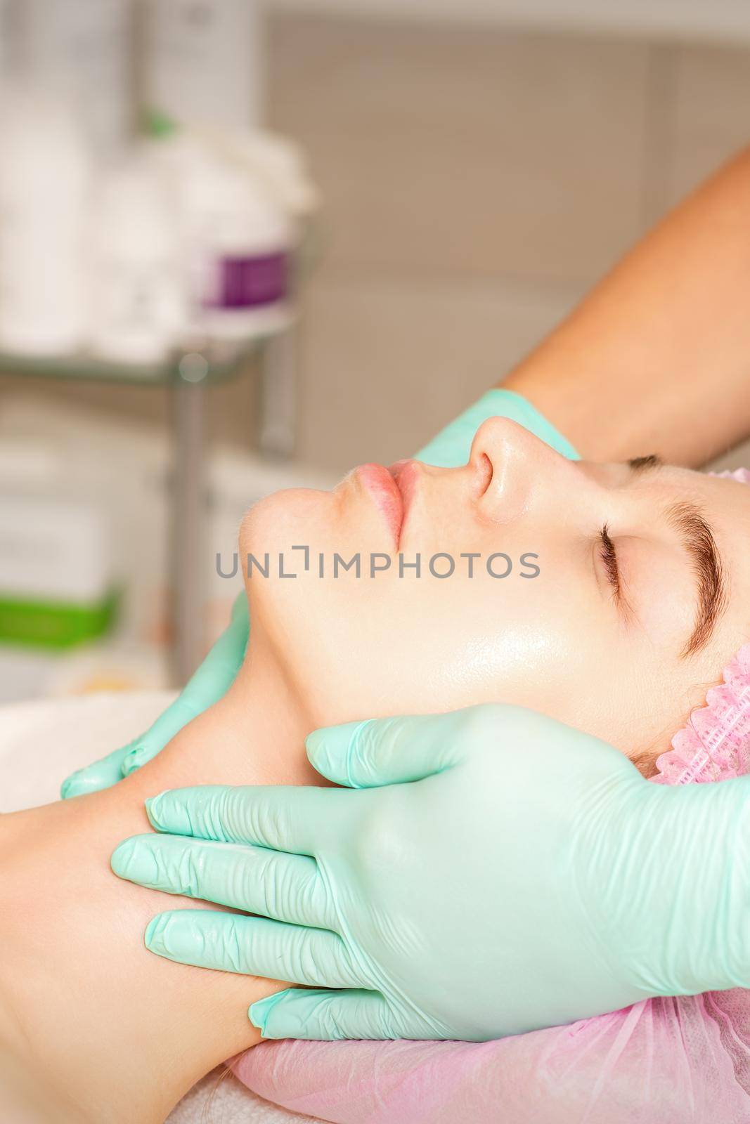 Cosmetologist with gloved hands applies a moisturizing mask with peeling cream on the female face. Facial cosmetology treatment. Procedures for facial care