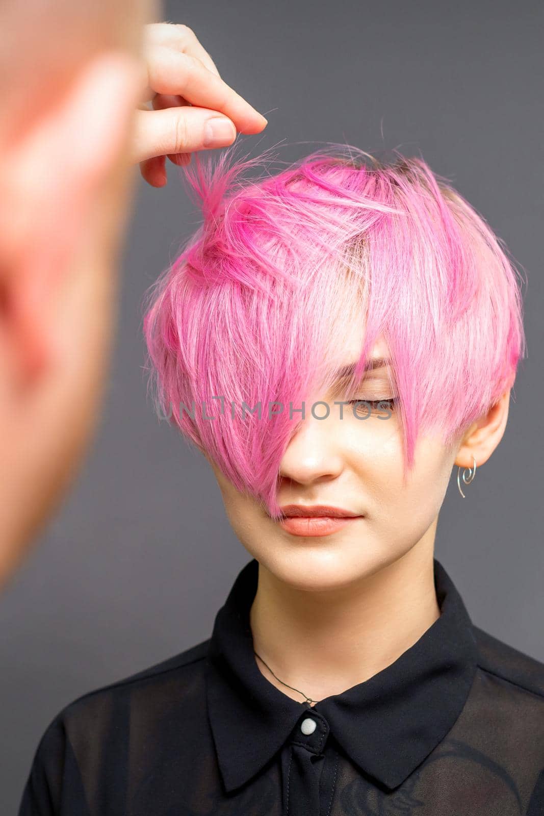 Hairdresser with hands is checking out and fixing the short pink hairstyle of the young white woman in a hair salon. by okskukuruza