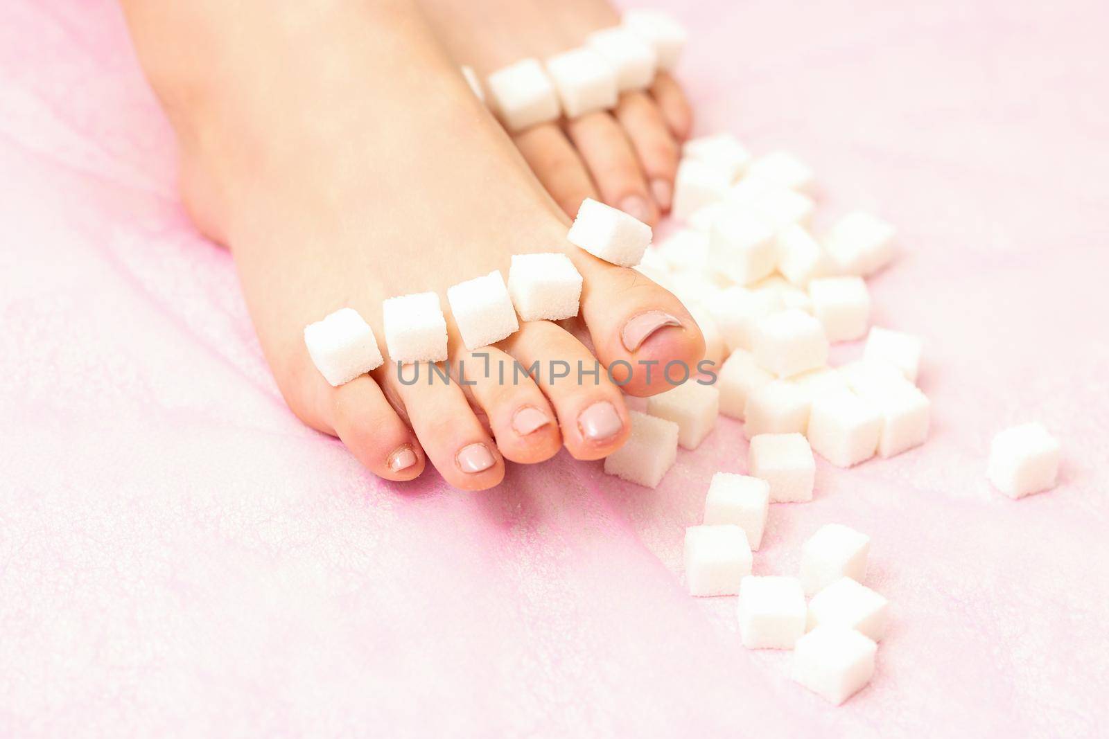 The concept of epilation, waxing. Sugar cubes lying down in a row on female feet, toes over pink background. by okskukuruza