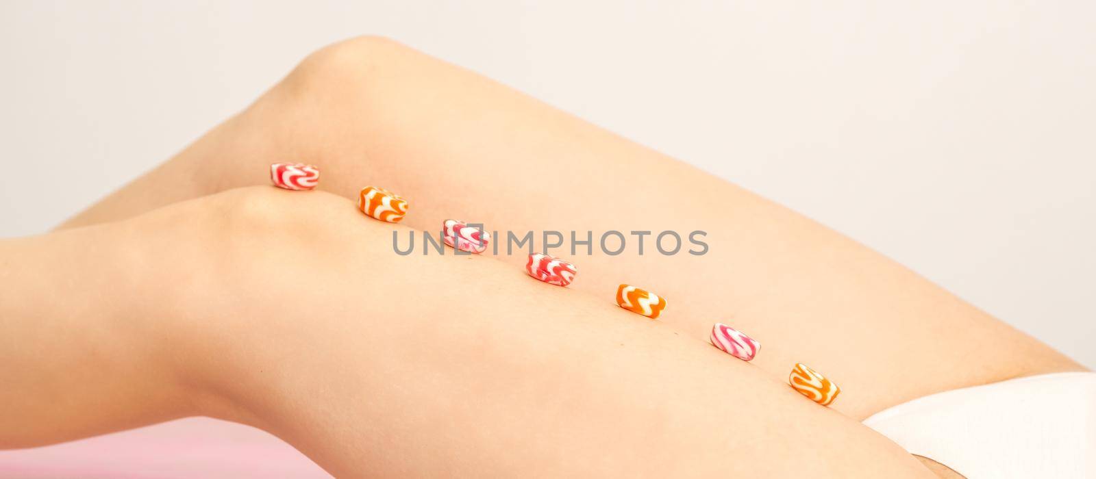 Depilation, waxing concept. Round candies lying down in a row on the female leg, close up. by okskukuruza