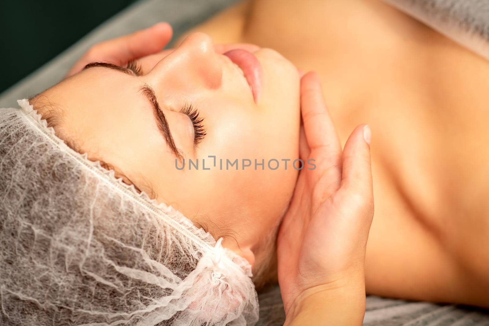 Facial massage. Hands of a masseur massaging neck of a young caucasian woman in a spa salon, the concept of health massage