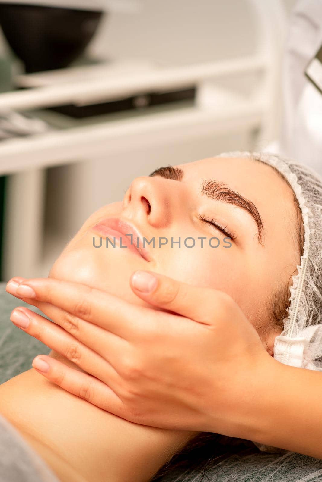 Facial massage. Hands of a masseur massaging neck of a young caucasian woman in a spa salon, the concept of health massage. by okskukuruza