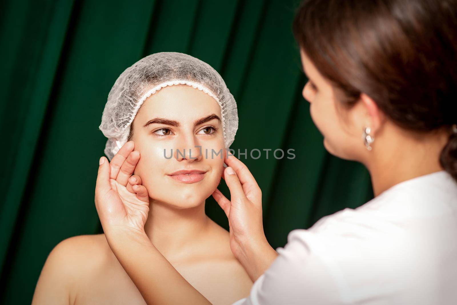 Plastic surgery and beauty concept. Professional cosmetician examining and touching the face of the beautiful young caucasian smiling woman in a clinic of esthetic cosmetology