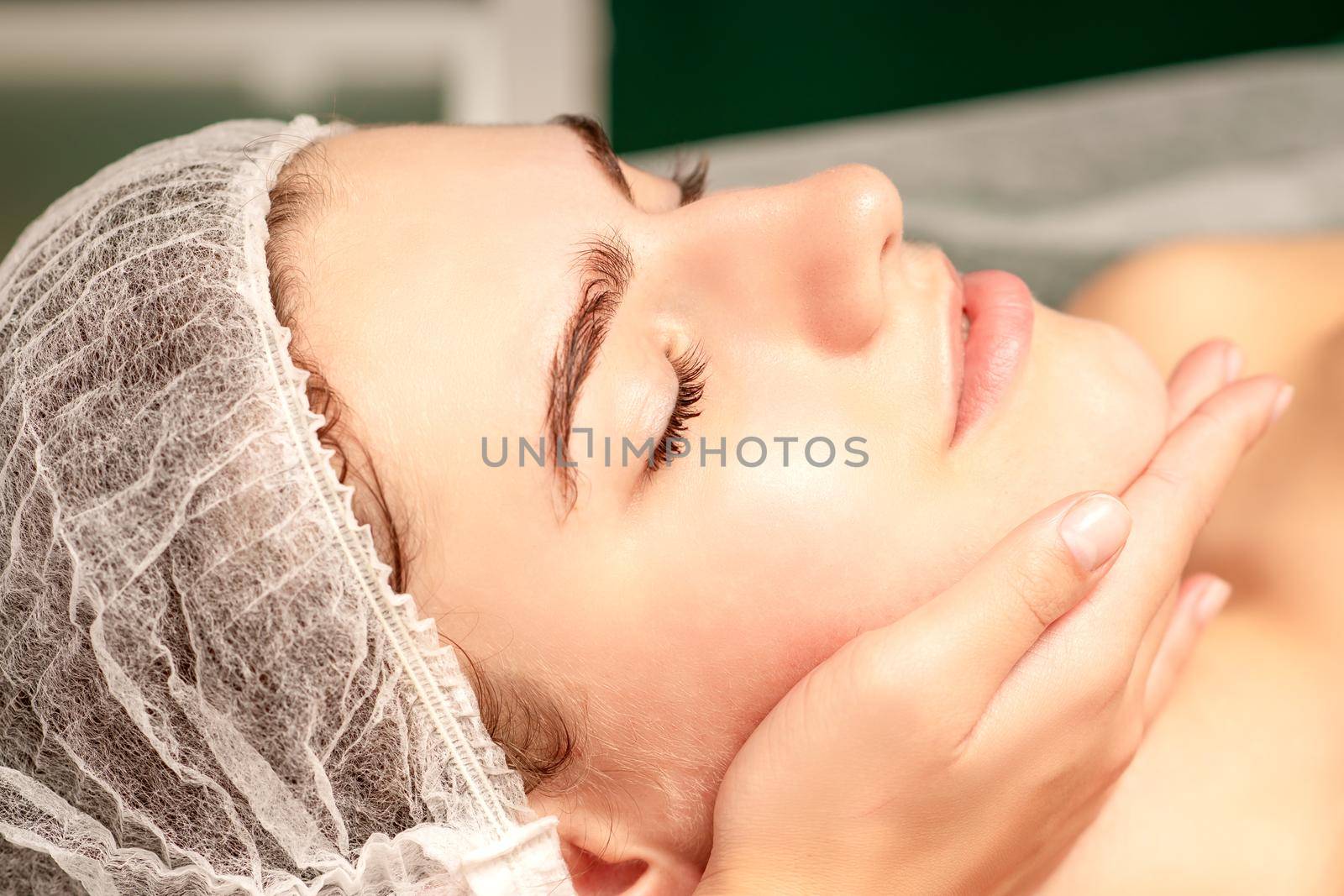 Facial massage. Hands of a masseur massaging neck of a young caucasian woman in a spa salon, the concept of health massage