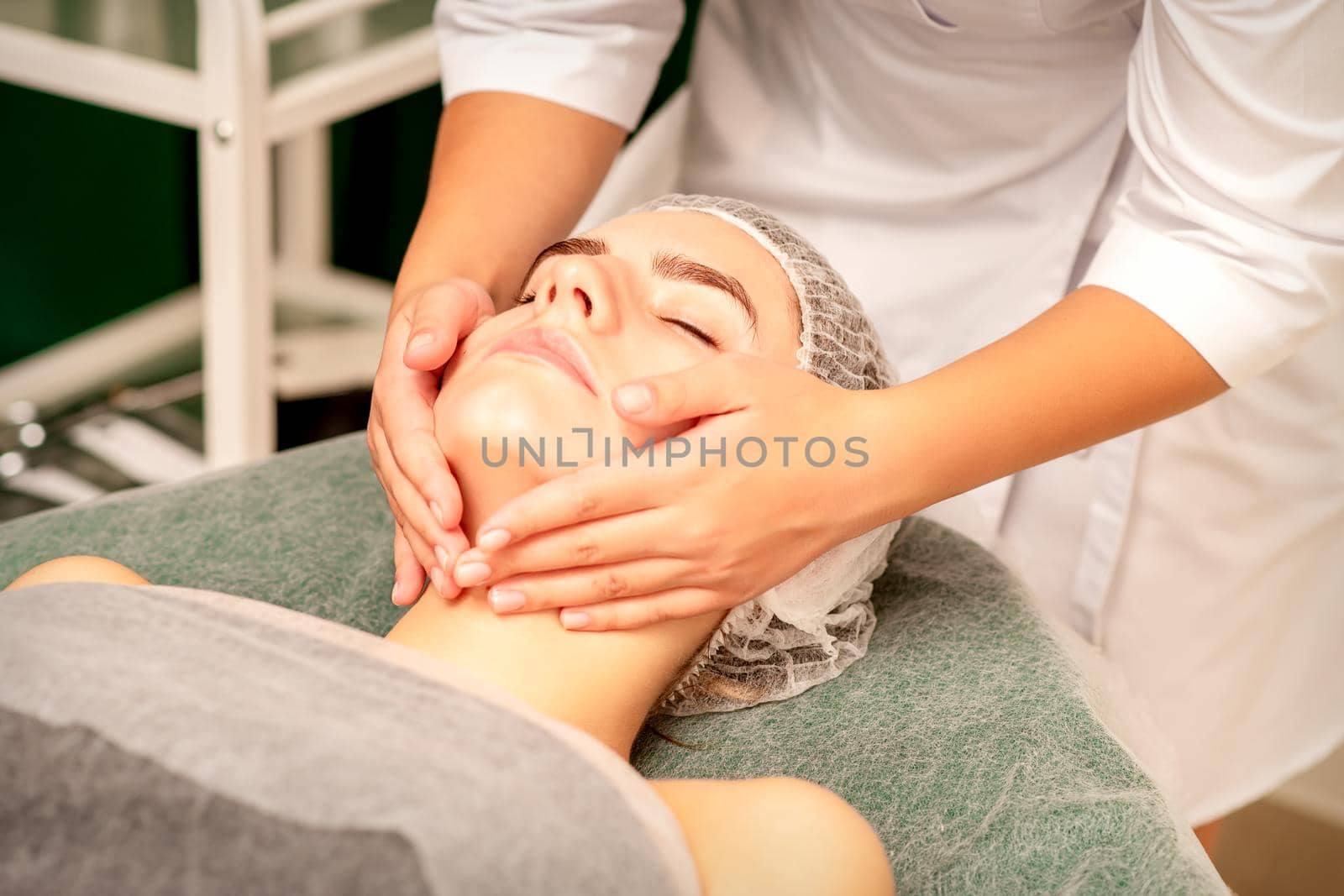 Facial treatment massage. Beautiful young caucasian woman with perfect skin receiving face and neck massage at a beauty spa