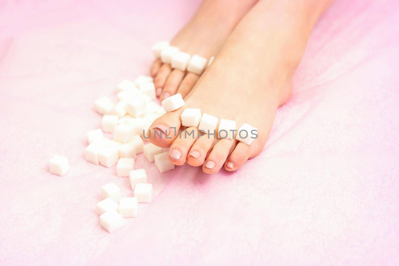 The concept of epilation, waxing. Sugar cubes lying down in a row on female feet, toes over pink background. by okskukuruza