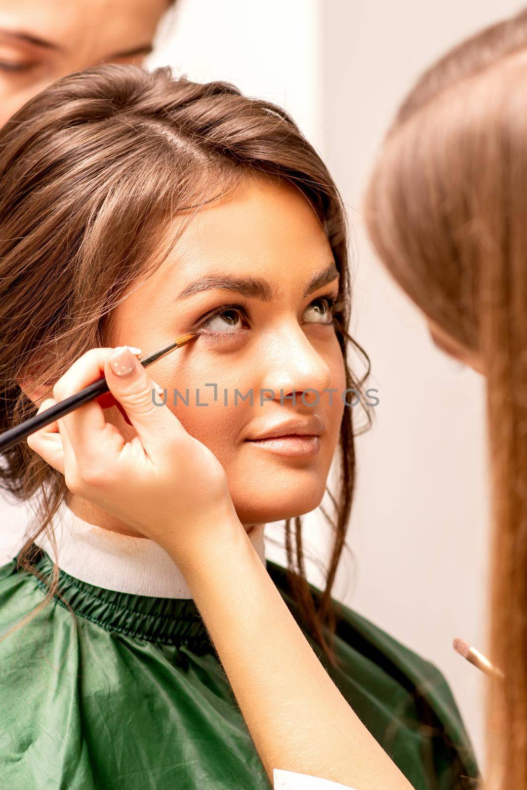 The makeup artist applies a concealer under the eyes using a makeup brush